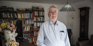 Wolfgang Rosenkötten steht in einer Wohnung vor einem Bücherregal