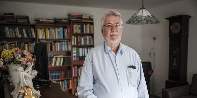 Wolfgang Rosenkötten steht in einer Wohnung vor einem Bücherregal