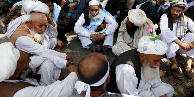Männer, die weiße Turbane tragen, sitzen auf dem Boden und unterhalten sich
