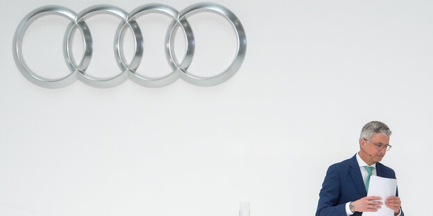 Rupert Stadler nimmt seine Papier und geht, im Hintergrund hängt ein großes Audi-Logo