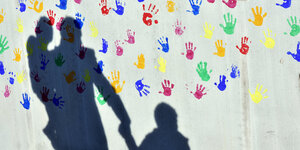 Schatten von Vater mit Kindern vor einer Wand, auf der lauter bunte Hände sind