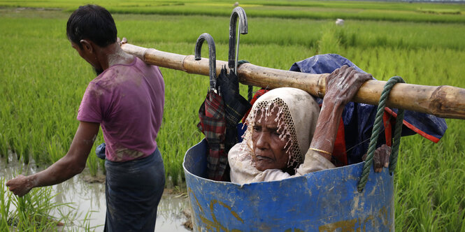 Flüchtlinge der Rohingya tragen eine alte Frau über einen schlammigen Weg, nachdem sie die Grenze zwischen Bangladesch und Myanmar überquert haben