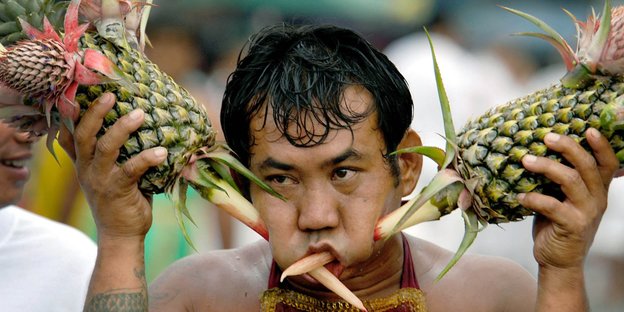 ein Mann, der sich mit Ananasspitzen Löcher in die Backen bohrt