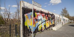 Ein abgebrochenes und mit Grafitto bespraytes Stück der Berliner Mauer trennt einen Weg und eine Brachfläche trennt