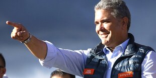 Iván Duque zeigt mit dem Zeigefinger nach links, im Hintergrund blauer Himmel