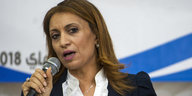 Souad Abderrahim kandidiert als Bürgermeisterin, sie trägt einen Anzug mit Rüschenhemd, die Haare offen und spricht in ein Mikrofon