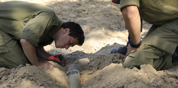 Zwei israelische Soldaten untersuchen eine Rakete, die sich in den Sandboden gebohrt hat