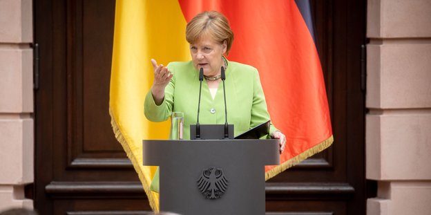 Bundeskanzlerin Angela Merkel am Rednerpult vor einer schwarz-rot-goldenen Fahne.