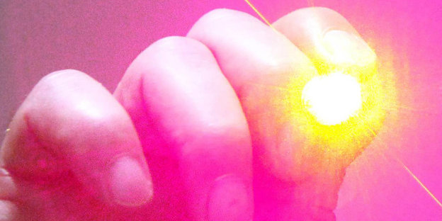 Eine Hand hält einen Laserpointer, aus dem grelles Licht kommt