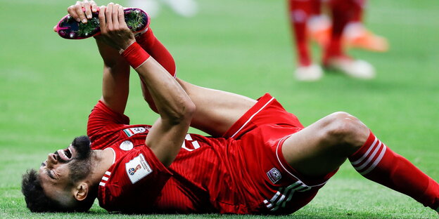 ein Fußballer liegt am Boden und hält sich den linken Fuß