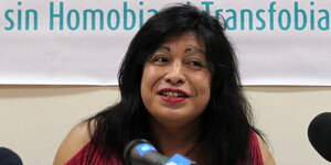 Eine Frau mit langen schwarzen Haaren spricht in ein Mikrofon