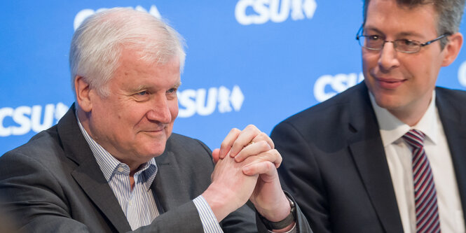 Horst Seehofer verschränkt lachend die Finger vor seiner Brust, Markus Blume sitzt neben ihm und sieht ihn an