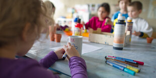 Ein Kind sitzt mit anderen Kindern an einem Tisch und malt