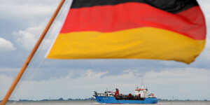 Ein Schiff fährt hinter einer Deutschlandflagge einen Fluss hinunter
