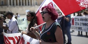 Eine Demonstrantin mit roten Haaren hält ein Transparent mit roter Schrift und eine rote Fahne