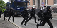 Behelmte Polizisten laufen beim G20-Gipfel neben einem Waserwerfer.