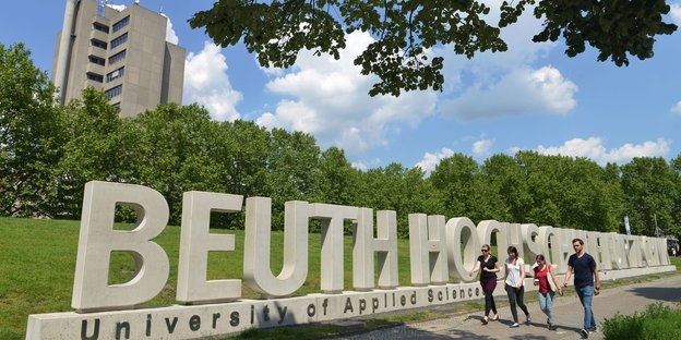 Studierende laufen vor dem Schriftzug Beuth-Hochschule durchs Grüne