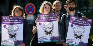 Zwei Frauen und ein Mann halten Plakate hoch, auf denen eine Person zu sehen ist, deren Mund zugeklebt ist. Auf dem Klebeband steht "Paragraf 219a"
