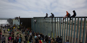 Menschen vor Grenzzaun am Meer, ein paar sitzen auf dem Zaun