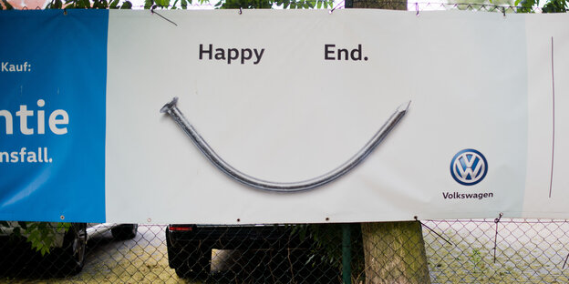Ein Zaun, an dem ein VW-Plakat mit der Aufschrift "Happy End" hängt