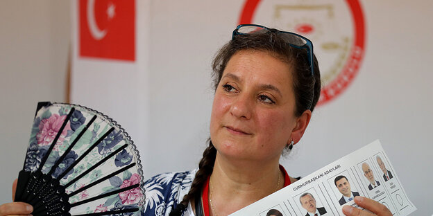 Türkei-Wahl in Deutschland - Frau hält Fächer und einen Wahlzettel in der Hand, hinter ihr die türkische Fahne