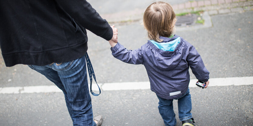 Eine Mutter hält ihr Kind an der Hand, beide sind von hinten zu sehen