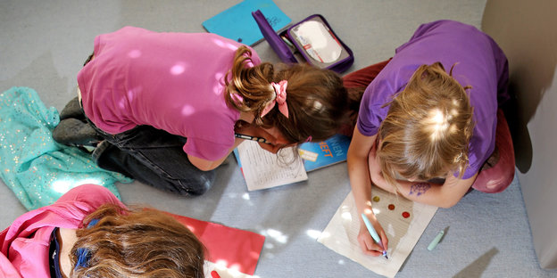 Drei Kinder hocken am Boden und schreiben in Schulhefte
