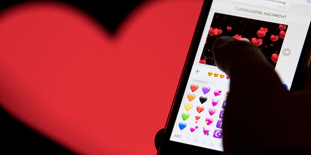 Ein rotes Herz im Hintergrund. Im Vordergrund ein Smartphone mit vielen Herz-Emojis drauf