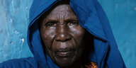 Porträt einer älteren schwarzen Frau mit blauem Kopftuch vor blauer Wand