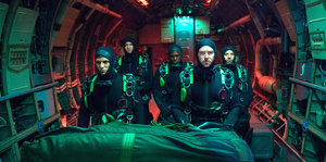 In einem U-Boot stehen fünf Navy-Seals in Taucheranzügen, oben leuchtet rotes Licht, vor den Personen liegt eine große Tasche