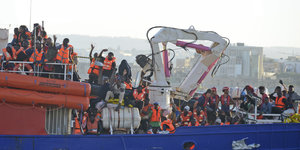 Auf einem Schiff drängen sich Menschen in orangenen Warnwesten und winken