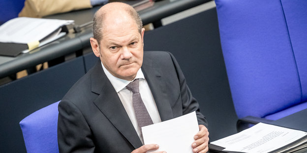 Der Bundesfinanzminister Olaf Scholz sitzt im Plenum des Bundestags und hält Papiere in der Hand