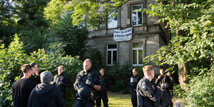 Mehrere Polizeibeamte mit Helmen und Schutzwesten stehen vor einem alten Haus