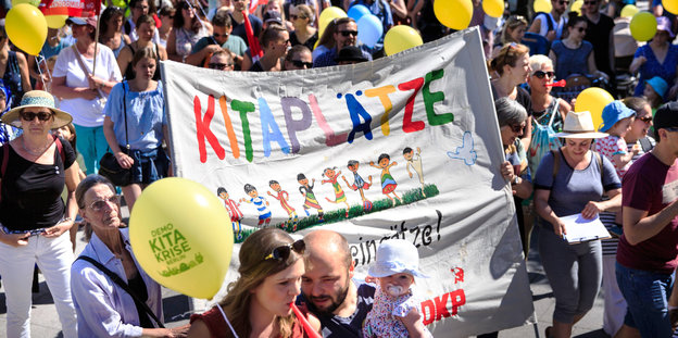 "Kitaplätze" steht bunt auf einem Tuch, dass Menschen bei der Eltern-Demo tragen