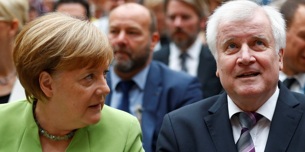 Merkel, im apfelgrünen Sakko, beugt sich fragend zum neben ihr sitzenden Seehofer, der guckt nach oben