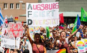 Demonstrant*innen halten in Augsburg bunte Schilder gegen die AfD hoch, unter anderem mit dem Slogan „Augsburg feiert Diversität“