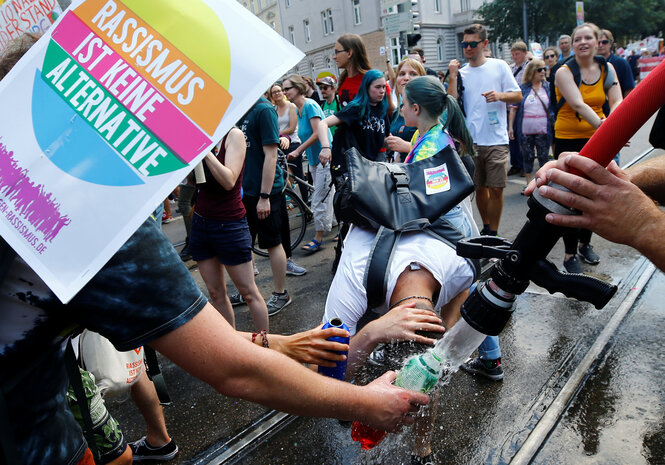 Demonstrant*innen holen sich Wasser aus einem Feuerwehrschlauch