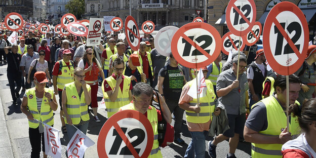Demonstranten laufen im Protest gegen den Zwölf-Stunden-Tag mit Schildern durch Wien, auf denen eine 12 durchgestrichen ist