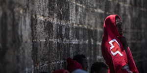 Ein Mann steht in eine rote Decke gehüllt vor einer Mauer