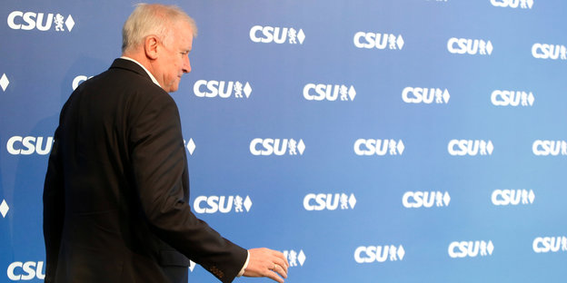 Horst Seehofer geht vor einer blauen Wand entlang, auf die das CSU-Logo als Muster gedruckt ist