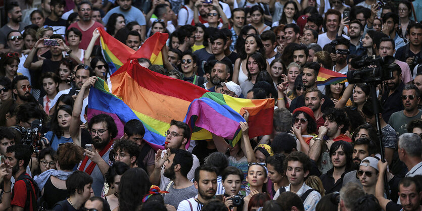 Viele Menschen stehen beieinander. Sie tragen eine bunte Flagge.