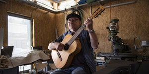 Karl Thiel sitzt mit seiner Gitarre in seiner Werkstatt