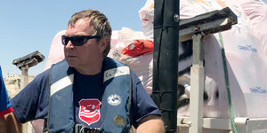 „Lifeline“-Kapitän Claus-Peter Reisch steht mit einer Rettungswesteam Wasser