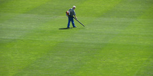 Ein Mann geht mit einem Laubbläser über ein Fußballfeld.
