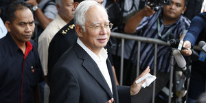 Najib Razak hebt leicht die Hände, an einem Gitter steht ein Kameramann