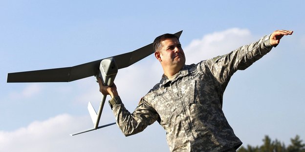 Ein US-Soldat hält eine Flugzeugdrohne in der Hand. Er befindet sich in Deutschlad. Er ist kurz davor die Drohne in Richtung Himmel starten zu lassen.