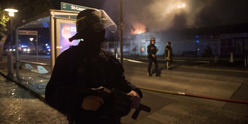 Ein Polizist steht mit Helm und Waffe bei Nacht auf einer Straße