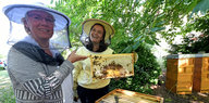 Barbara Otte-Kinast steht neben einer Frau, die einen Bienenstock in den Händen hält