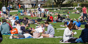 Menschen sitzen auf Decken und Jacken auf dem Boden einer Grünanlage
