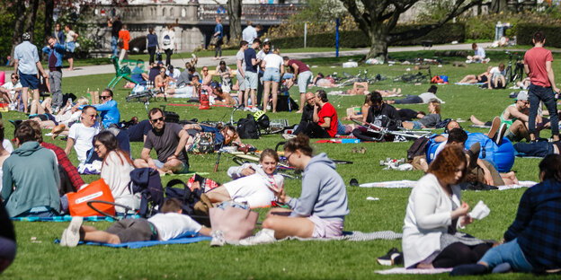Menschen sitzen auf Decken und Jacken auf dem Boden einer Grünanlage